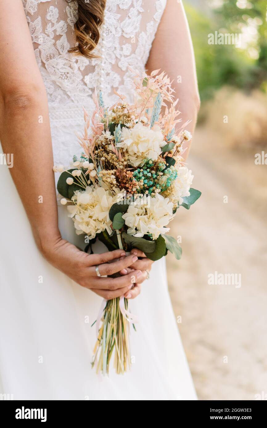 Una donna irriconoscibile nel suo abito da sposa tiene un bouquet nuziale di fiori conservati nelle sue mani. Foto Stock