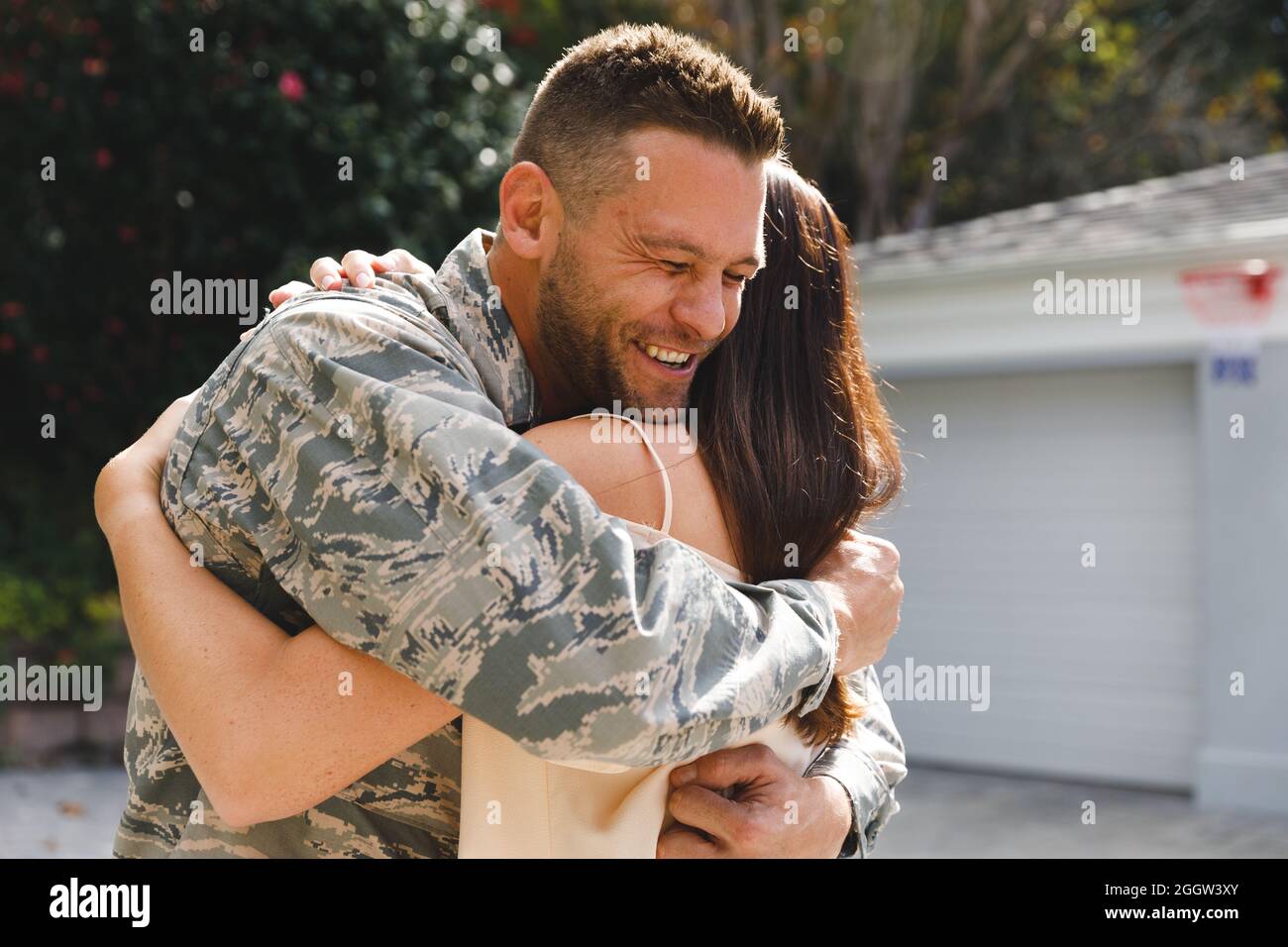Soldato maschio caucasico che abbraccia la moglie fuori casa decorata con la bandiera americana. Soldato di ritorno a casa in moglie. Foto Stock