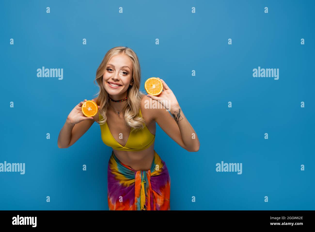 giovane donna sorridente in cima bikini giallo che tiene metà arancione su blu Foto Stock