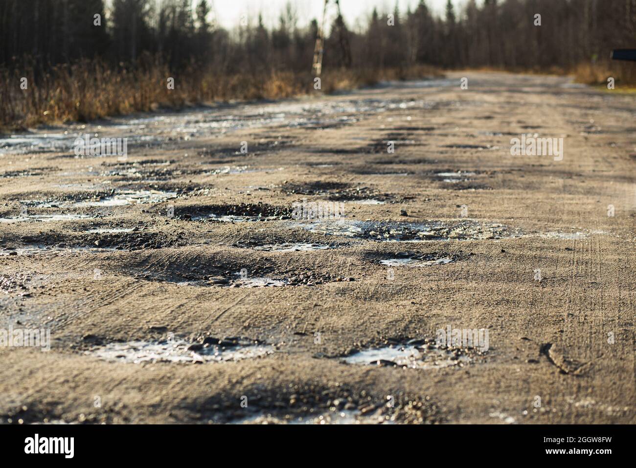 Autunno strada ghiaia sporca con buche coperte di gelo. Presenta alcuni danni superficiali, necessita di manutenzione, patch dei fori, polvere che si inceppa e si trascina. Il Foto Stock