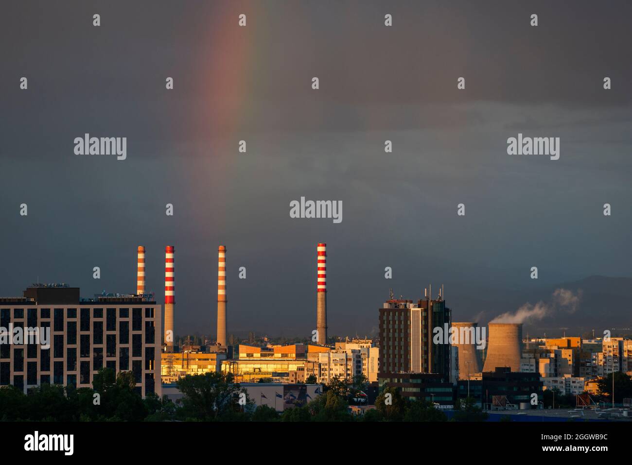 Camini delle centrali elettriche e arcobaleno luminoso contro il cielo scuro dopo la tempesta su un complesso industriale in ambiente urbano, Sofia Bulgaria, Europa orientale, Balcani, UE Foto Stock