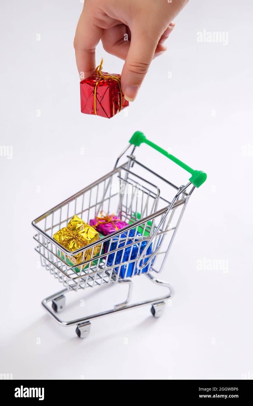 Una mano umana che mette una scatola del regalo in un carrello dei regali di shopping. Foto Stock