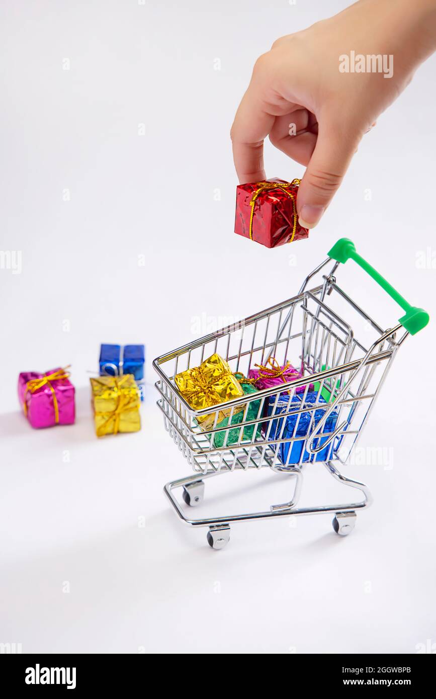 Una mano umana che mette una scatola del regalo in un carrello dei regali di shopping con le scatole del regalo tenute accanto. Foto Stock