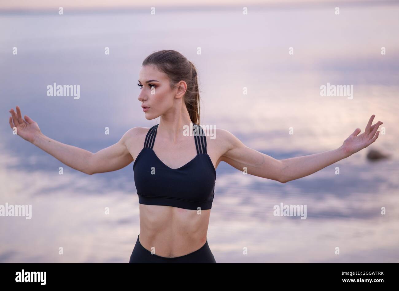 giovane ragazza bella scaldarsi prima di fare yoga sulla riva al tramonto Foto Stock