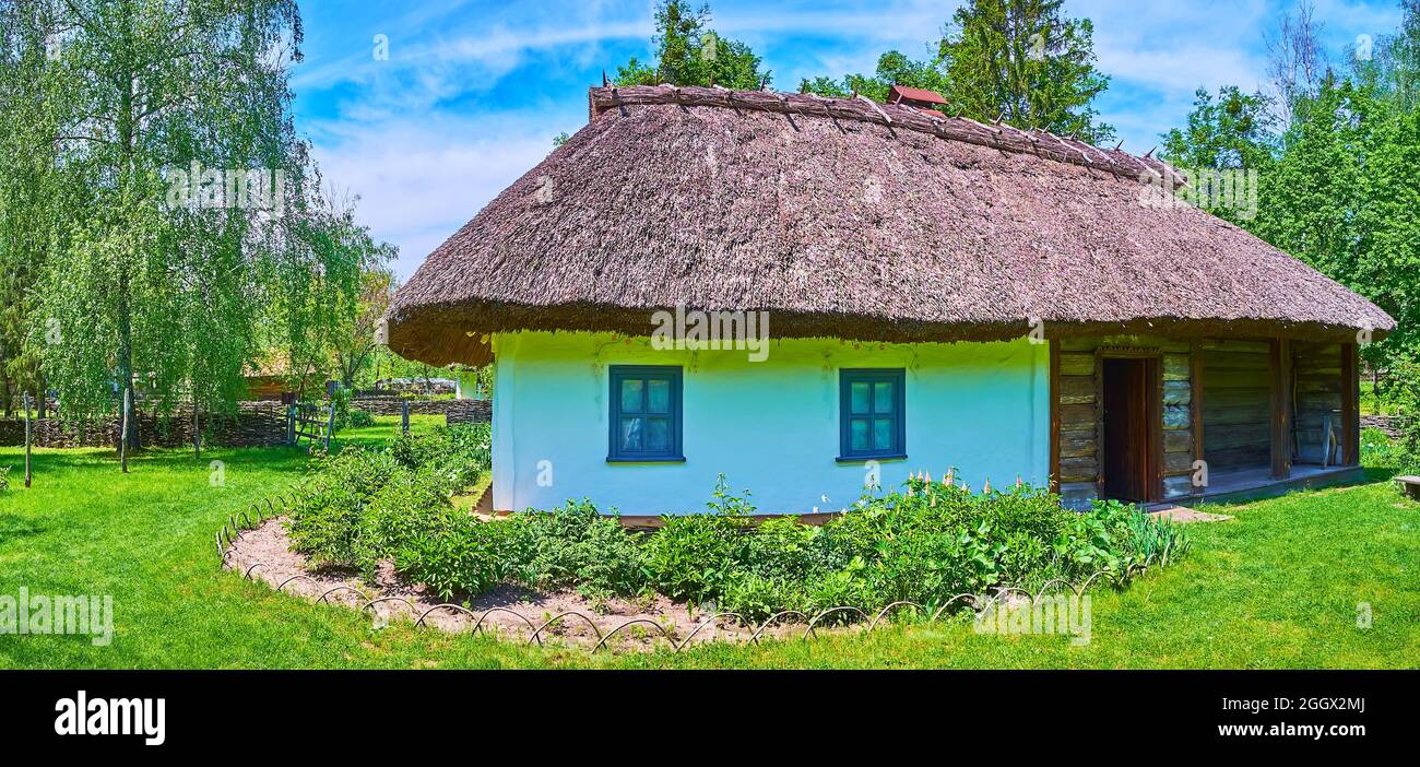 Panorama della casa medievale hata con tetto di paglia e il giardino con prato verde intorno, Pereiaslav Scansen, Ucraina Foto Stock