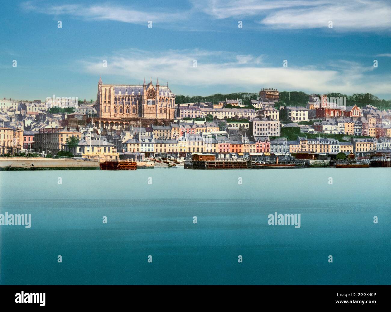 Una vista dei primi del 20 ° secolo della Chiesa Cattedrale di St Colman, aka Cattedrale di Cobh, torreggiante sopra le case terrazzate in Cobh, County Cork, Irlanda. La costruzione è iniziata nel 1868 e la fotografia illustra l'edificio prima dell'erezione del campanile esistente. Progettato dagli architetti Edward Welby Pugin e George Ashlin, non fu completato fino a oltre mezzo secolo dopo a causa degli aumenti dei costi e delle revisioni dei piani originali Foto Stock