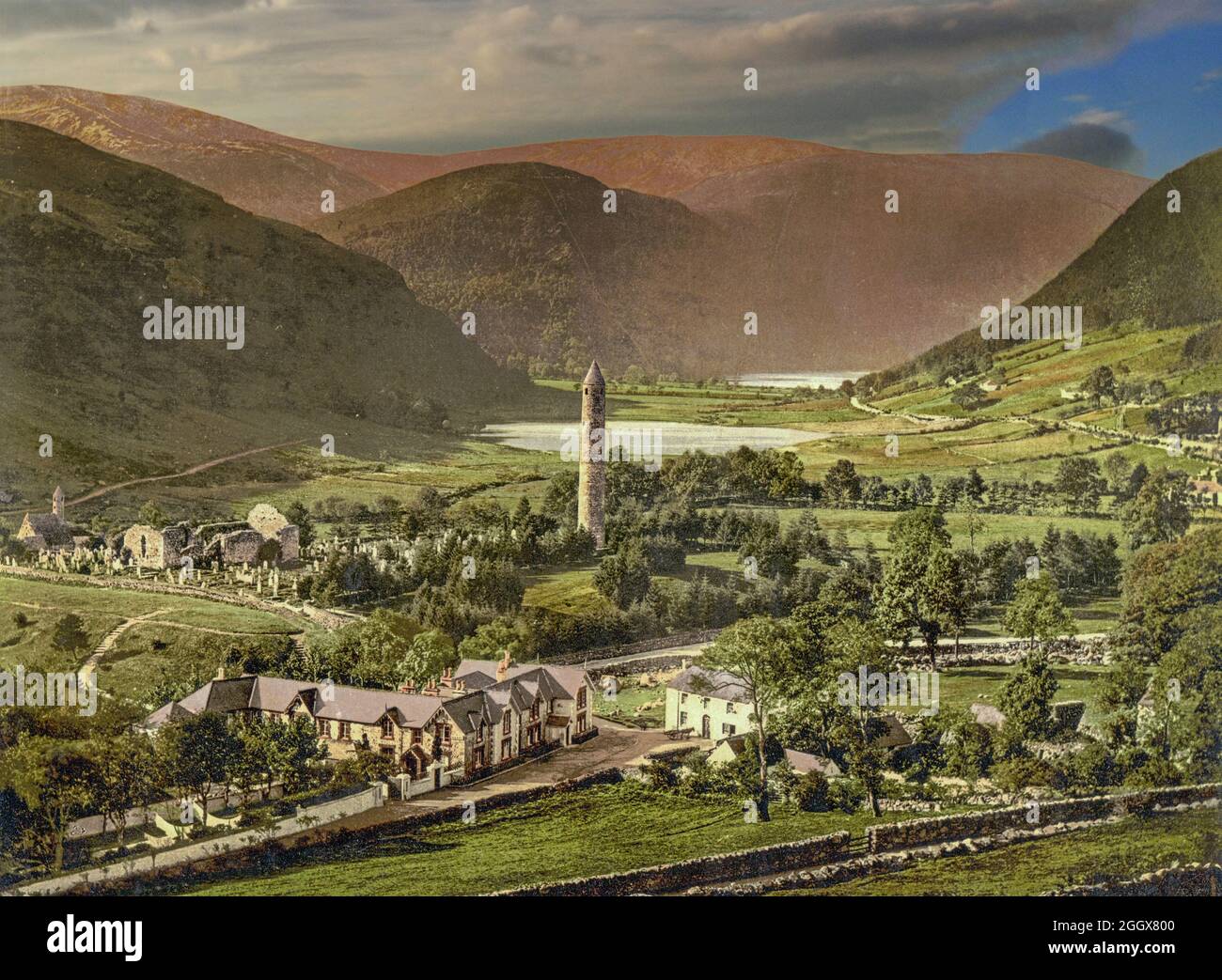 Una vista dei primi anni del XX secolo di Glendalough, una valle glaciale nella contea di Wicklow, in Irlanda, rinomata per un insediamento monastico medievale fondato nel VI secolo da St Kevin, un discendente di una delle famiglie dominanti di Leinster. La torre rotonda, alta circa 30 metri, ha funto da punto di riferimento per i visitatori in avvicinamento, torre campanaria, e a volte come deposito-casa e luogo di rifugio in tempi di attacco. Foto Stock