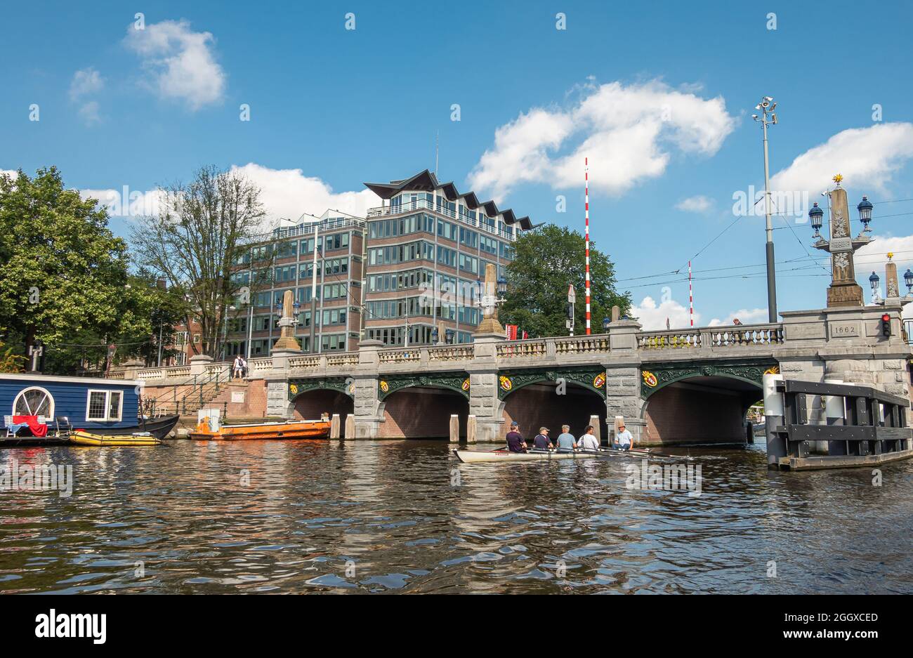 Amsterdam, Paesi Bassi - 15 agosto 2021: Hogesluis ponte in pietra sul fiume Amstel con canoa sotto il paesaggio azzurro. McKinsey e l'ufficio di vetro della società Foto Stock