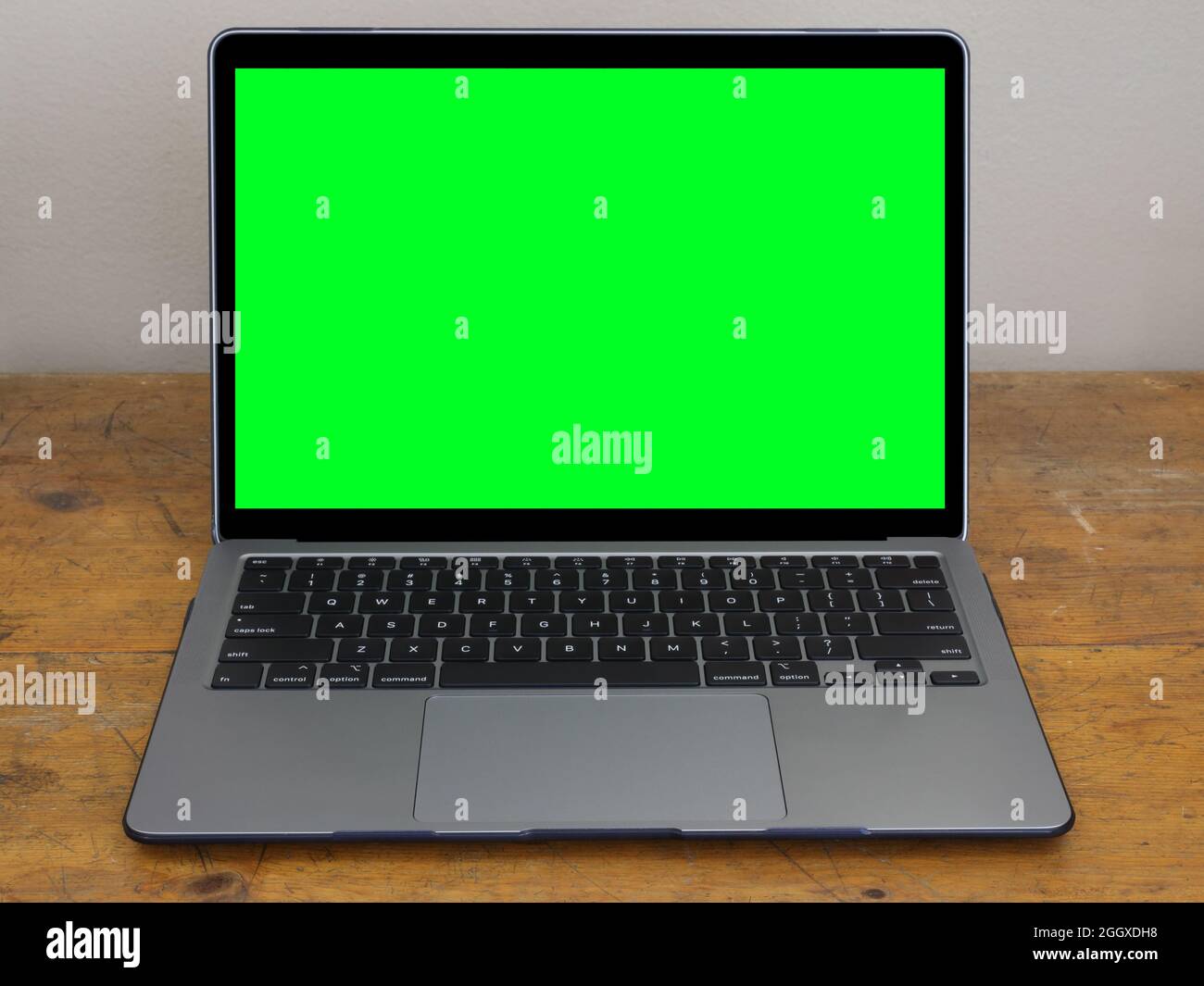 Un moderno computer portatile è mostrato isolato su una vecchia scrivania in legno da ufficio, con uno schermo verde sul monitor per aggiungere la vostra grafica. Foto Stock