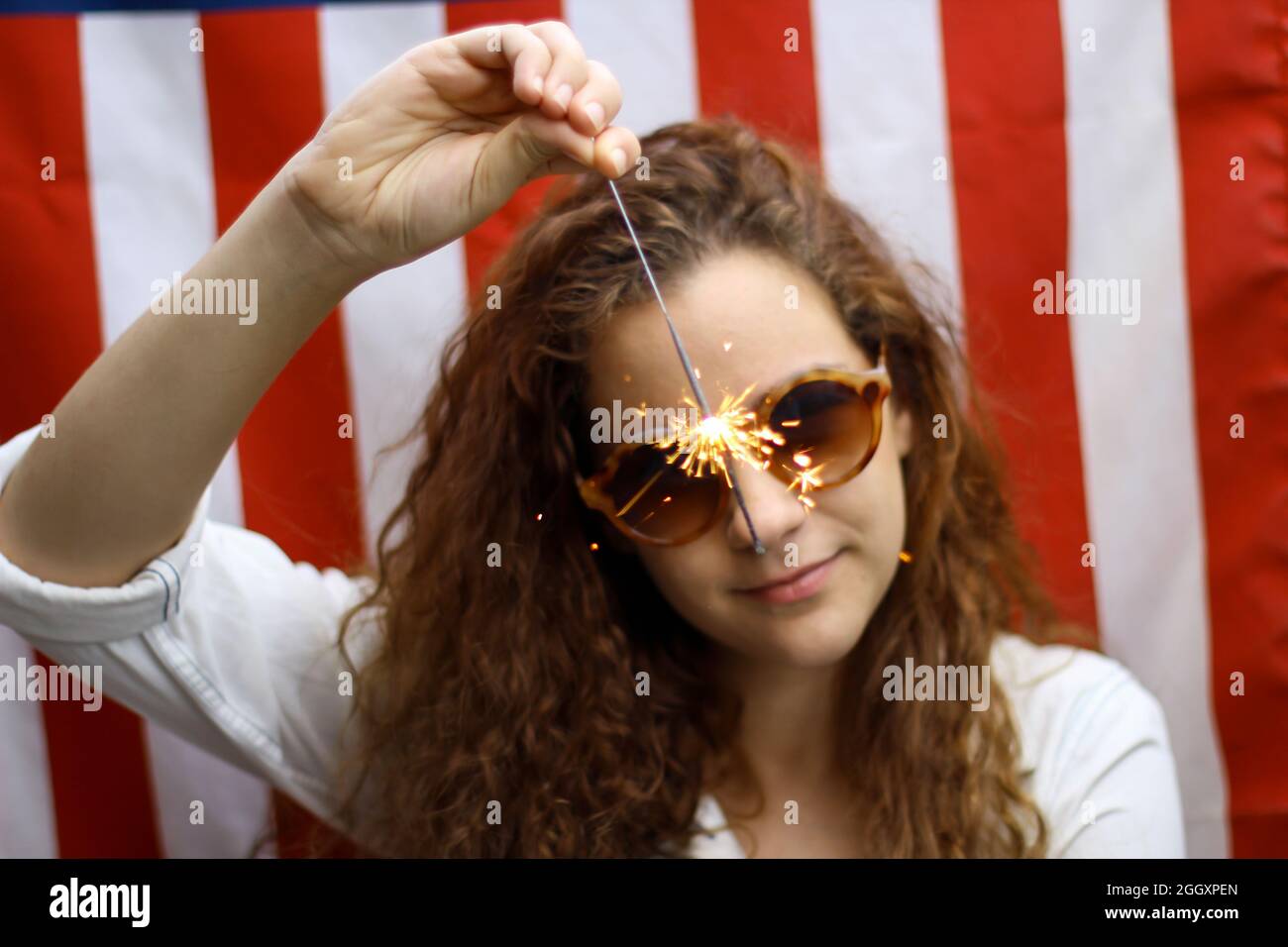 Giovane rosso ispanico e caucasico che tiene uno scintillio in piedi di fronte alla bandiera americana. Foto Stock