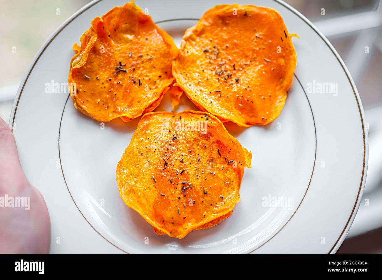 Macro closeup di persona che tiene piatto bianco con zucca butternut squash crudo ravioli ripieni disidratati alimenti italiani con fette, oliva extra vergine Foto Stock