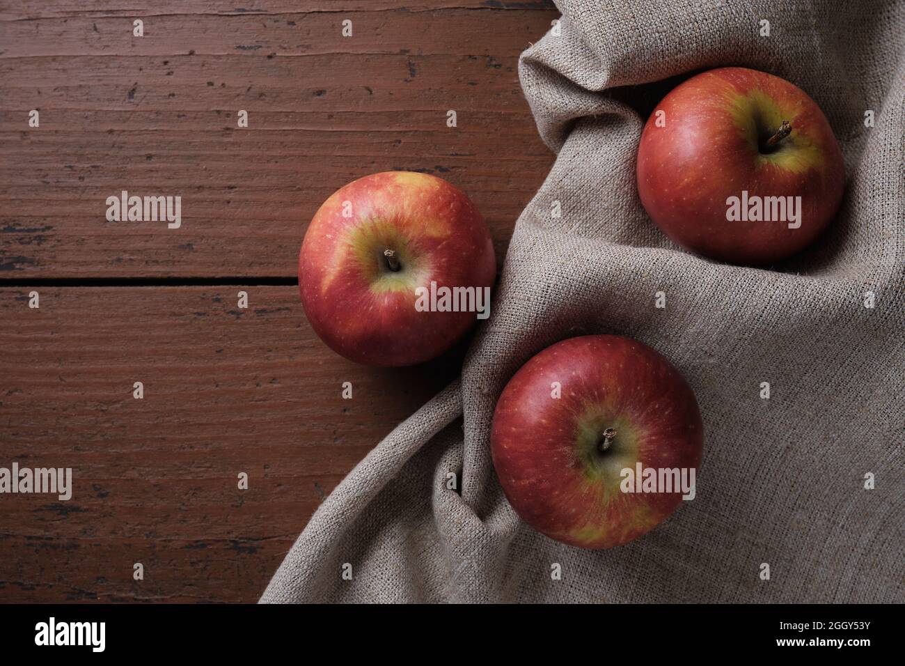 Frutta in una tovaglia di lino su un vecchio tavolo di legno. Mele su sfondo rosso scuro. Tema Apple Harvest. Posiziona per testo, vista dall'alto Foto Stock