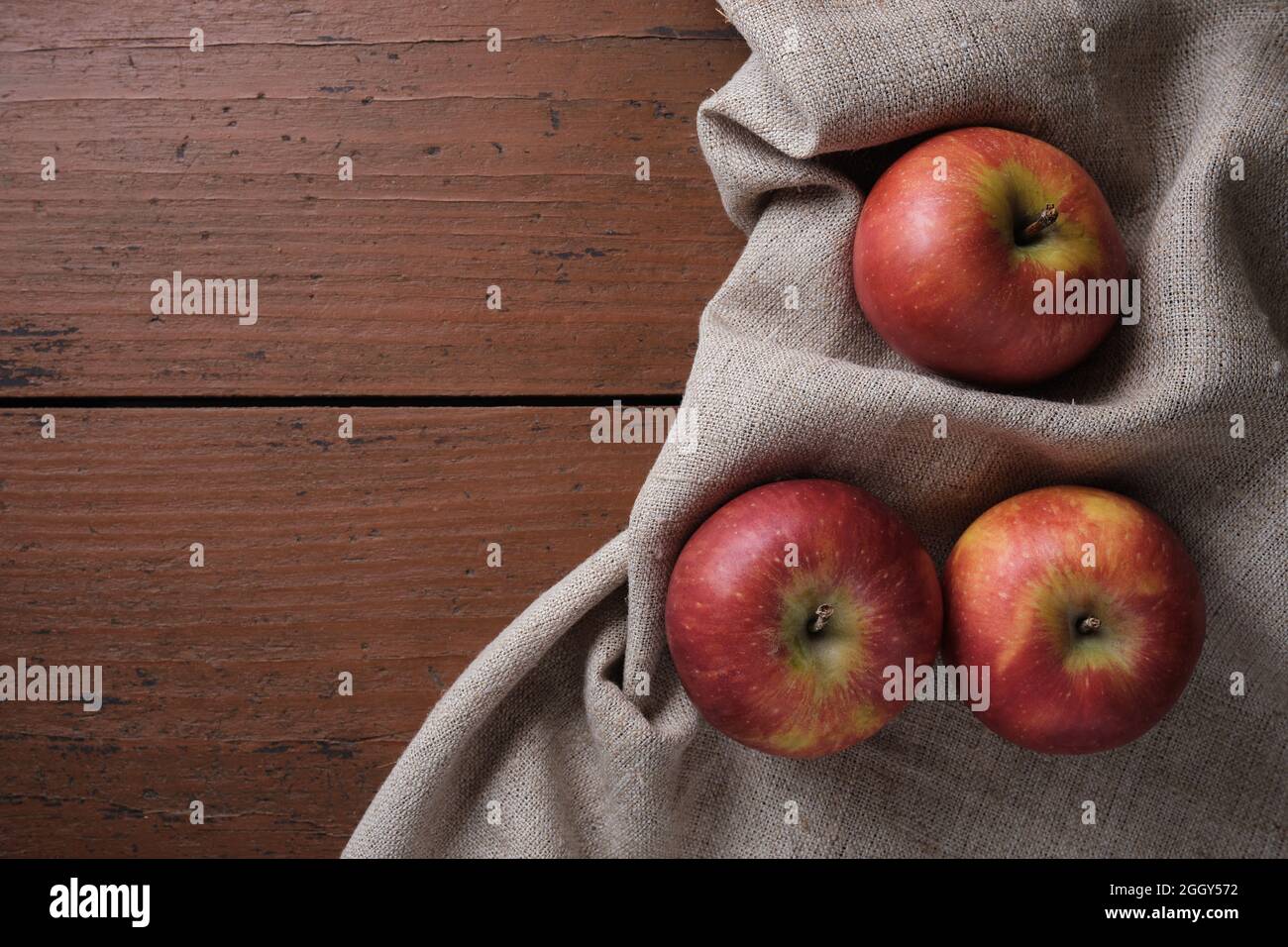 Frutta in una tovaglia di lino su un vecchio tavolo di legno. Mele su sfondo rosso scuro. Tema Apple Harvest. Posiziona per testo, vista dall'alto Foto Stock