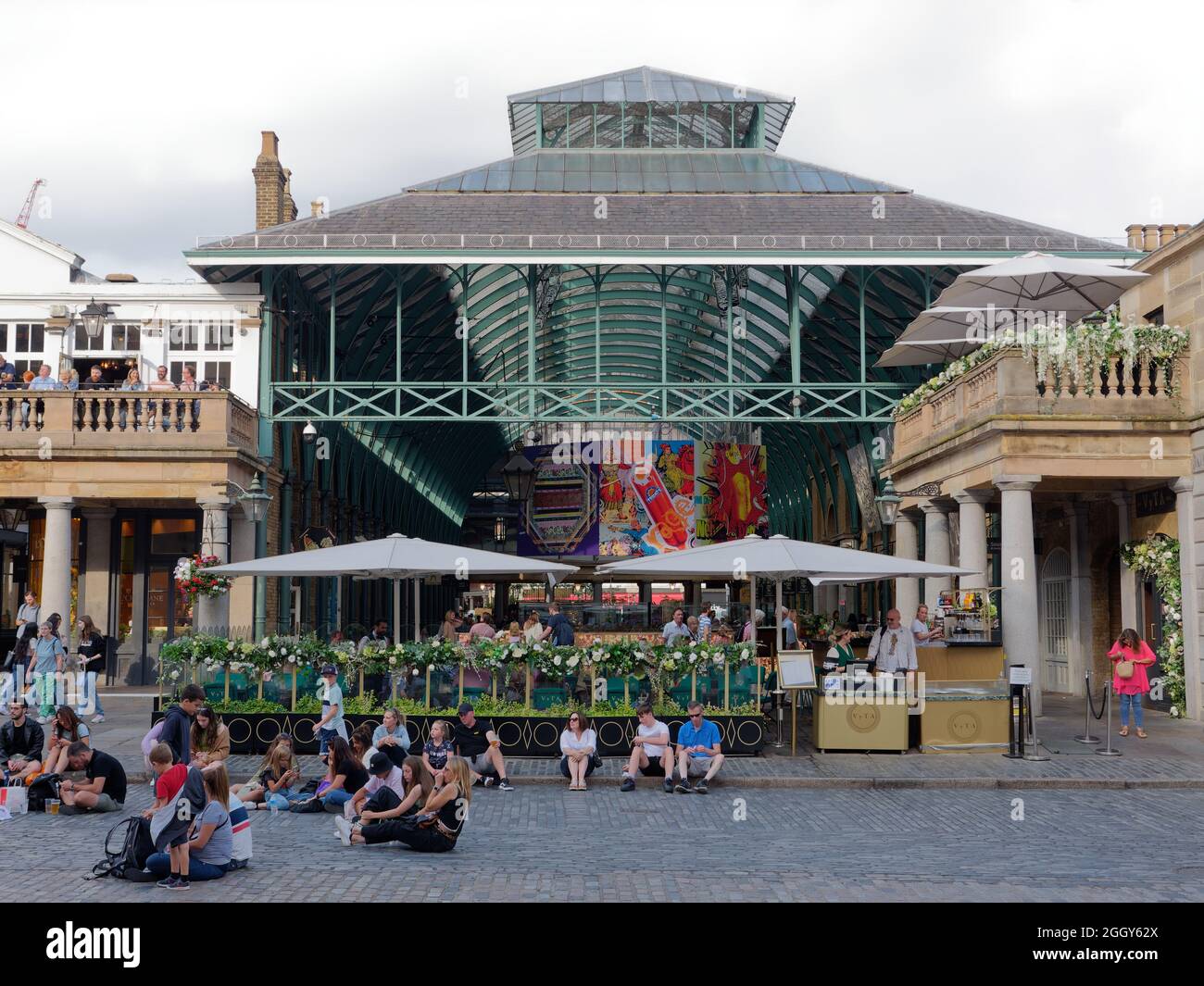 Londra, Grande Londra, Inghilterra, agosto 24 2021: La gente si siede sulla piazza principale a Covent Garden di fronte al suo mercato coperto. Foto Stock