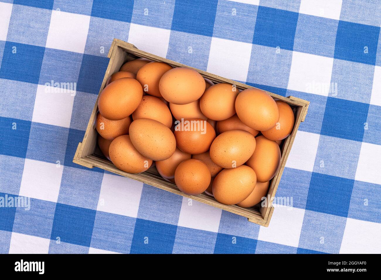 Una piccola cassa di uova di gallina marroni raccolte di fresco si riposa su una tradizionale tovaglia da picnic a scacchi blu e bianco. Foto Stock