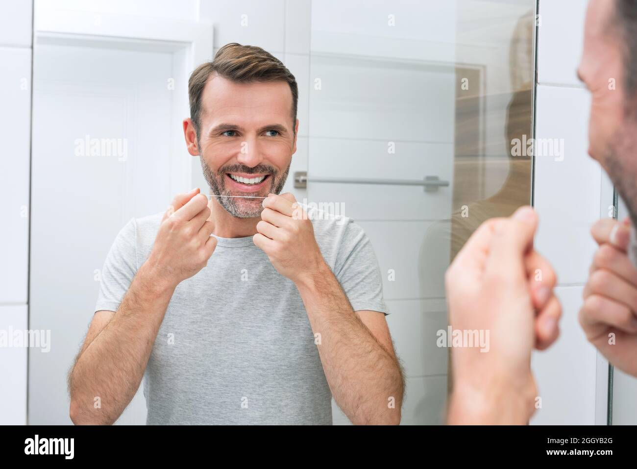 Uomo che usa il filo interdentale in bagno. Denti bianchi e un bel sorriso, concetto di igiene del mattino Foto Stock