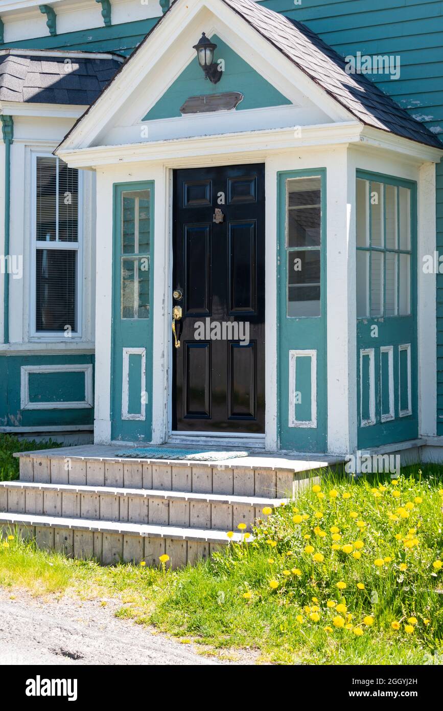 L'esterno di un edificio in legno verde teale di stile coloniale vintage con finiture decorative bianche. C'è una vecchia porta in legno nero con maniglie in ottone. Foto Stock
