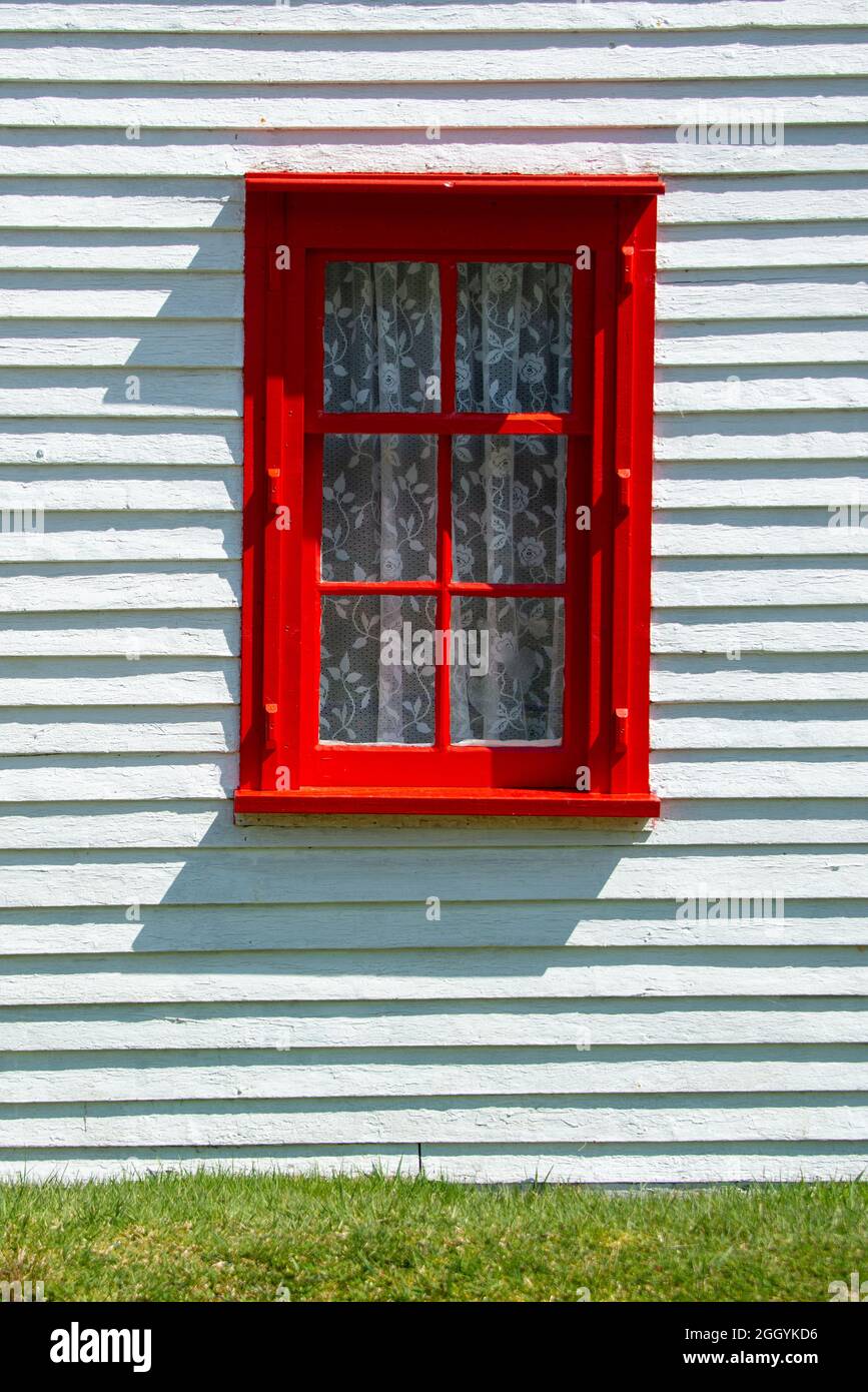 Una finestra vintage a doppia appesa rossa brillante con quattro vetri con tende in pizzo bianco. La finestra residenziale si trova all'esterno. Foto Stock