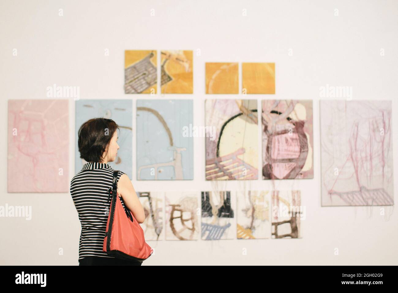 Donna asiatica in piedi in una galleria d'arte di fronte a colorati dipinti incorniciati esposti su una parete bianca Foto Stock