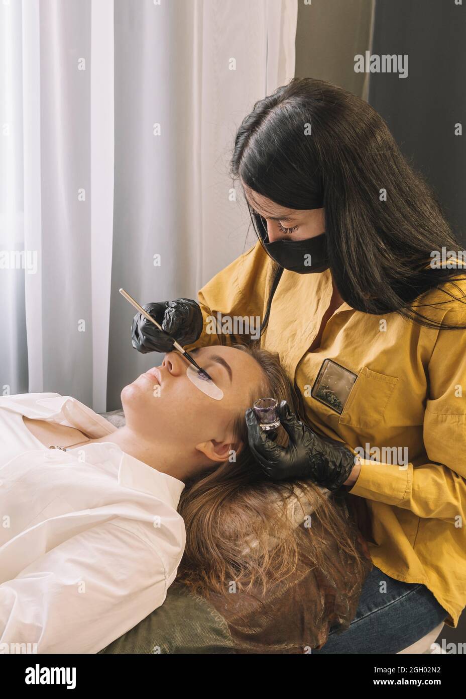 Donna sulla procedura cosmetica al salone. Una ragazza in un salone di bellezza sulla procedura di colorare le sue ciglia. Cura per sopracciglia e ciglia. Foto Stock