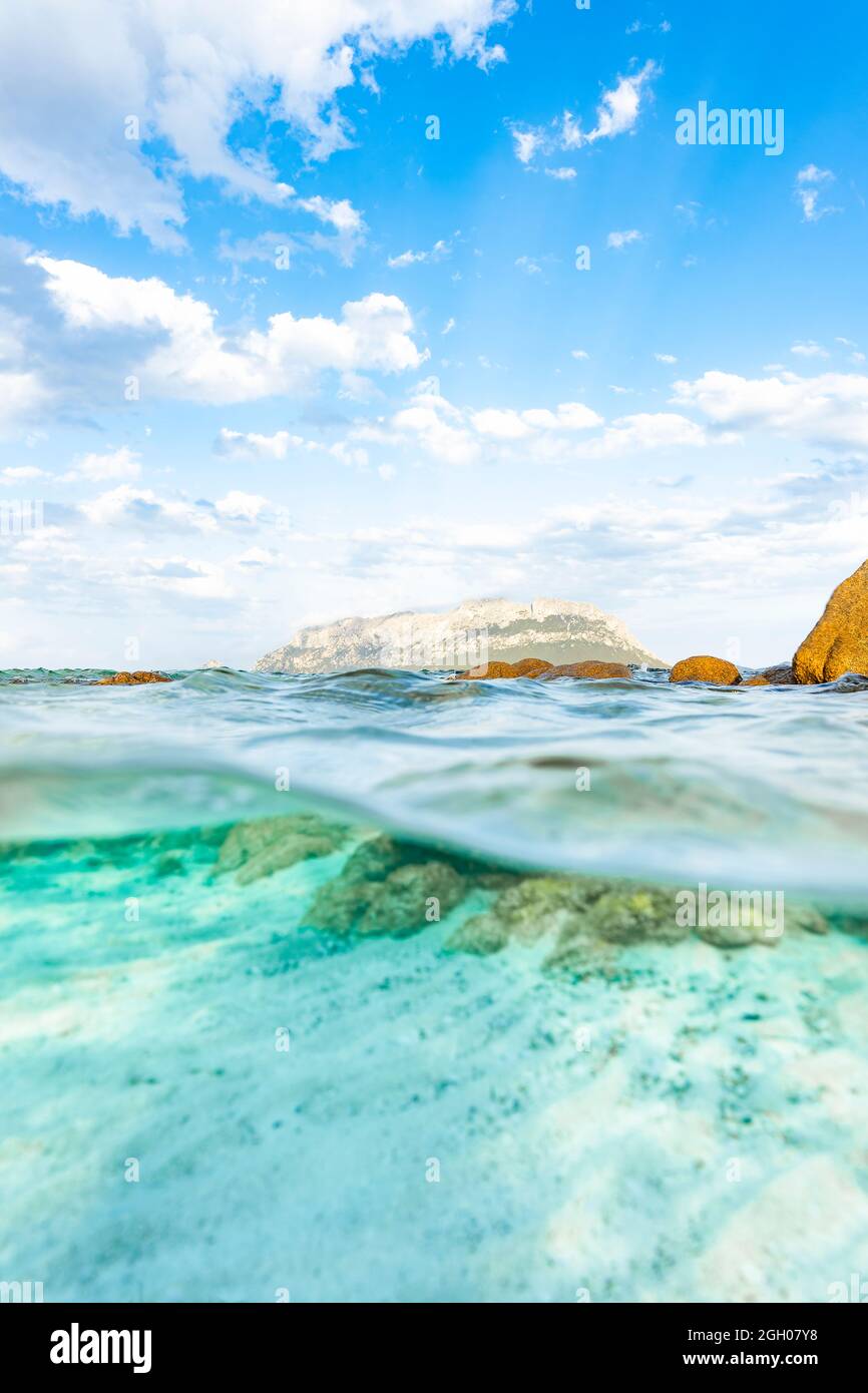 (Messa a fuoco selettiva) Split-shot, over-under shot, half in half out. Acque cristalline e turchesi in primo piano e Tavolara Island in lontananza. Foto Stock