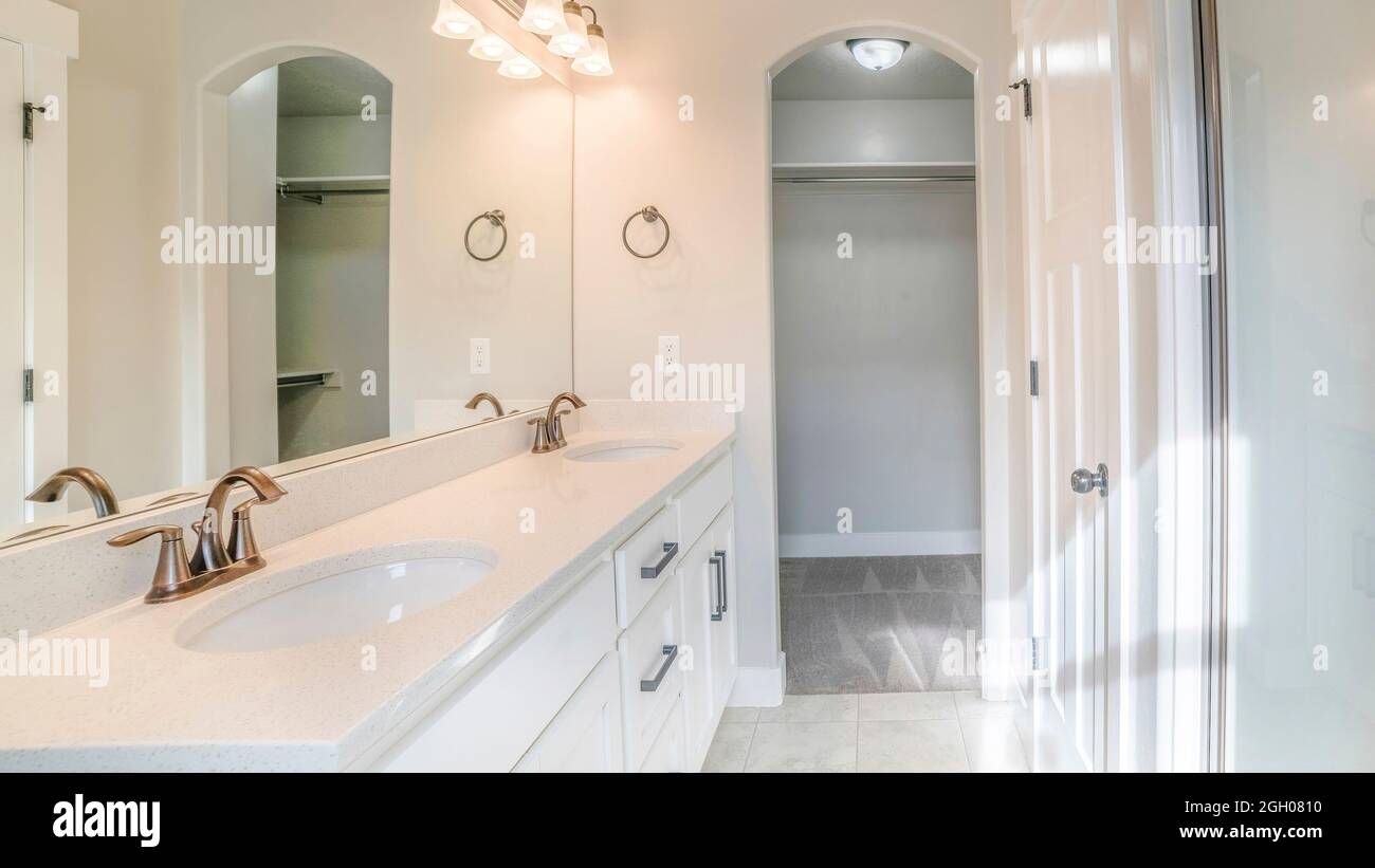 Pano interno di un bagno bianco con doccia con parete in vetro, lavandino e armadio vuoto Foto Stock