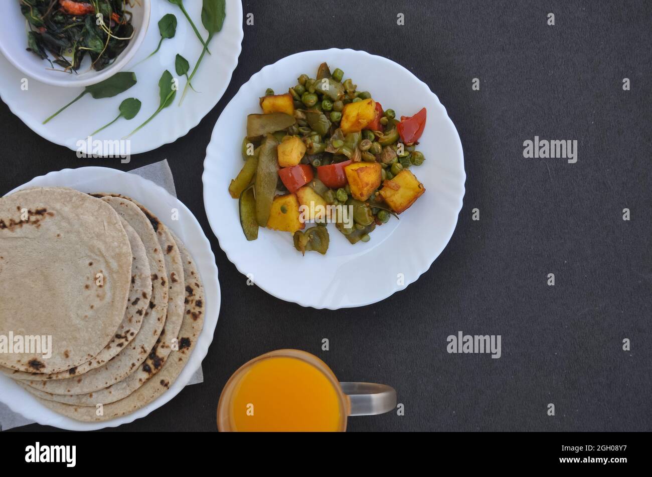 Piatto di paneer matar mix Veg, saag (verdi) e chapati (pane indiano) su piatti bianchi e succo su vetro su sfondo nero con spazio copia Foto Stock