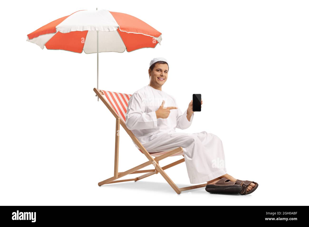 Giovane uomo in abiti etnici seduti sotto ombrello e puntando ad un telefono cellulare isolato su sfondo bianco Foto Stock