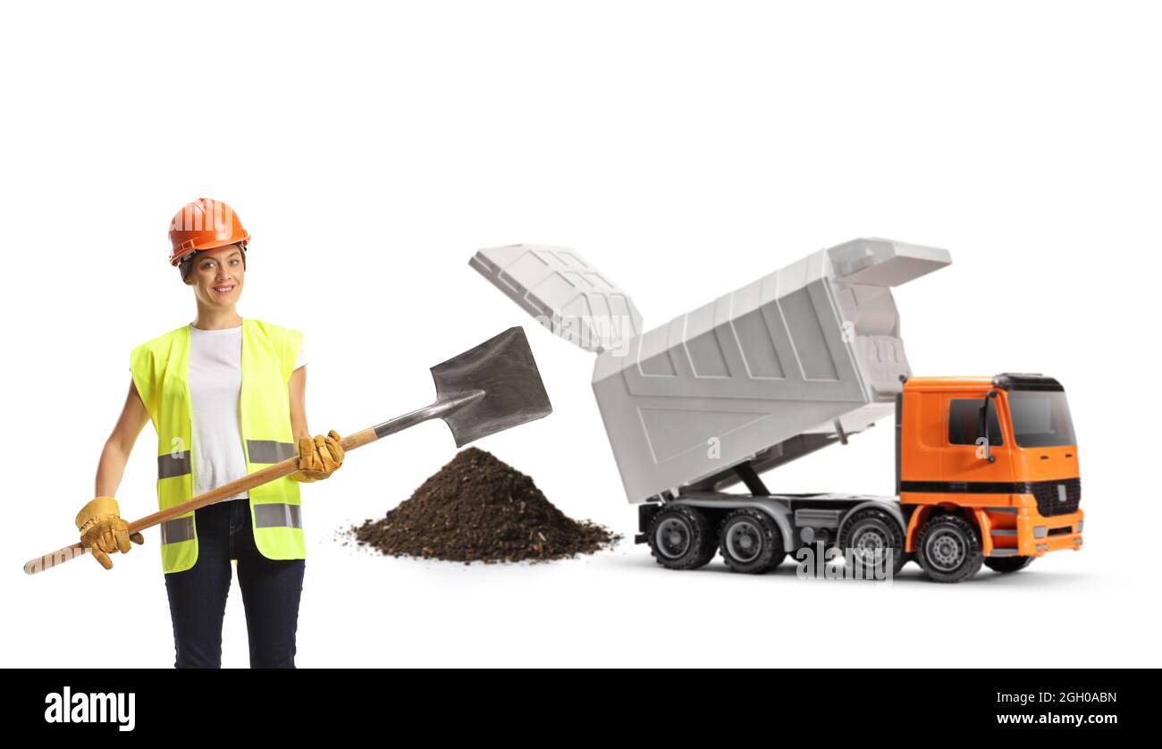 Lavoratore di costruzione femminile con un gilet e un hardhat che tiene una pala di fronte a un camion di scarico isolato su sfondo bianco Foto Stock