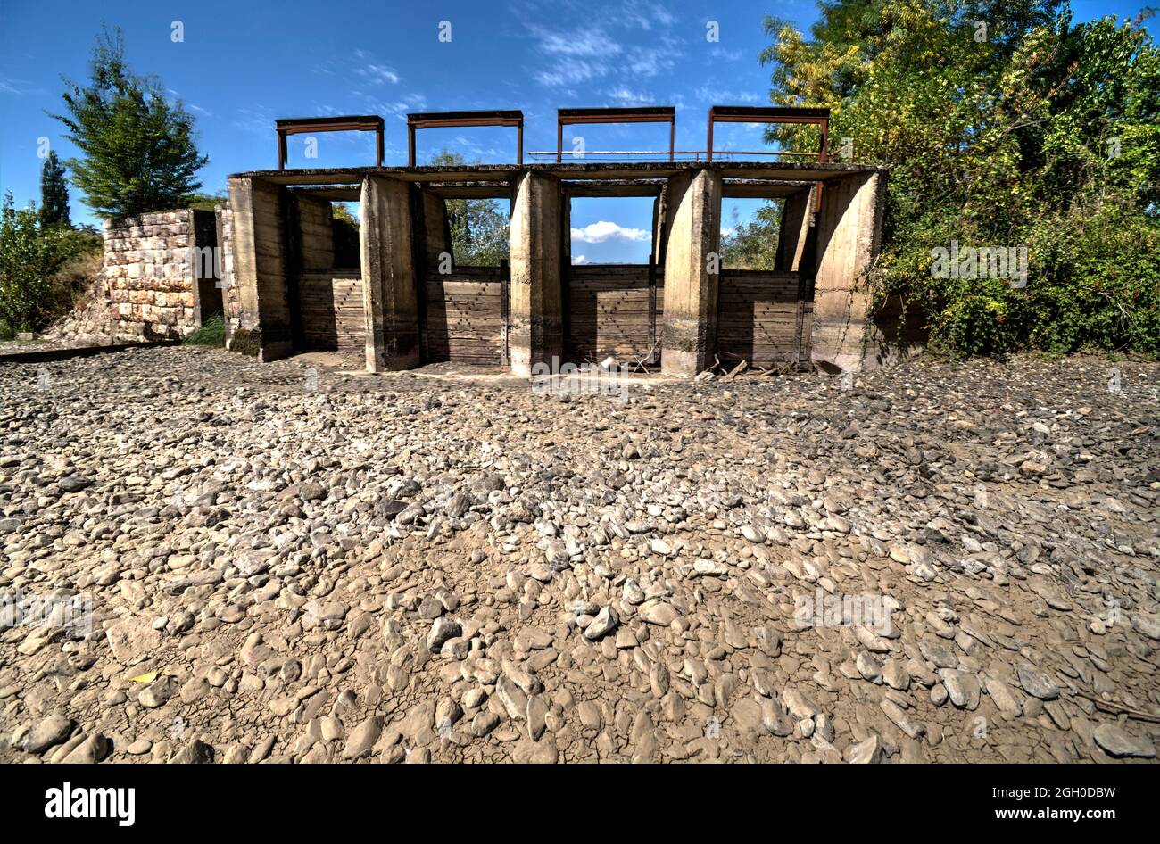 Il letto del fiume senza acqua, la siccità prende il suo pedaggio. Il letto del fiume è lastricato di pietre. Diga per la regolazione dell'acqua. Foto Stock