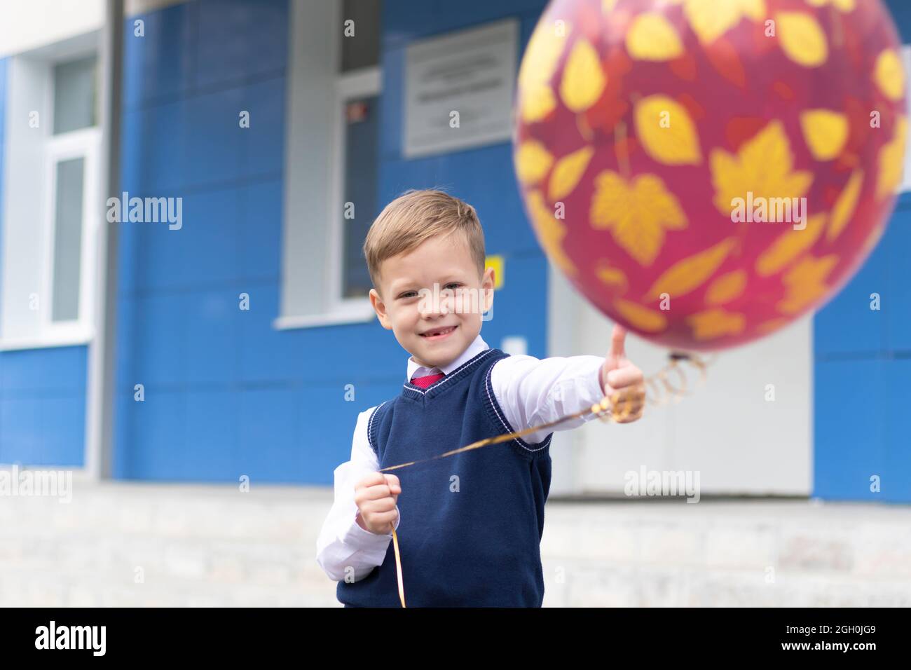 Ragazzo carino prima livellatore a scuola con un pallone in mano in una giornata di sole autunno. Celebrazione il 1 settembre. Giornata della conoscenza. Messa a fuoco selettiva Foto Stock