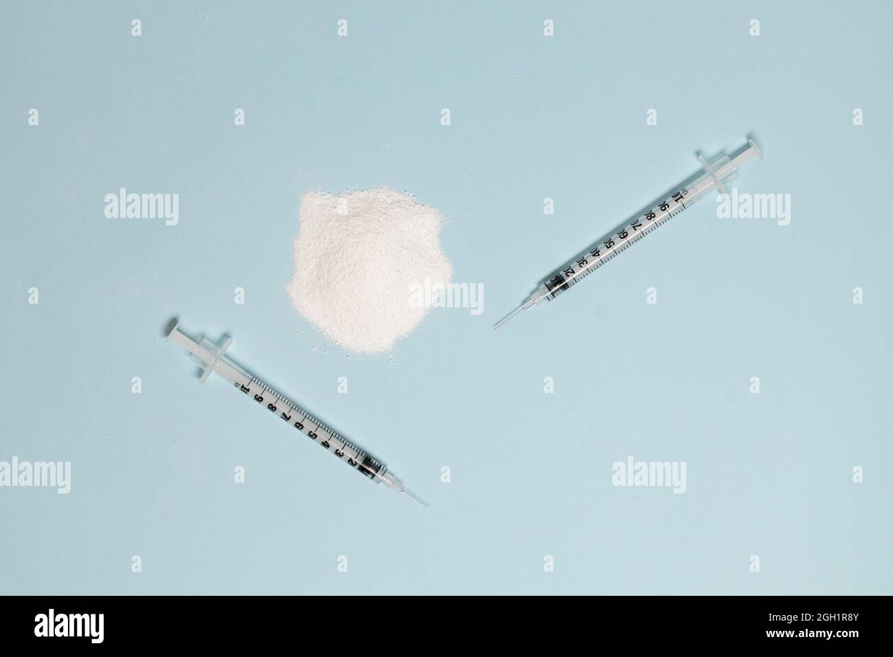 Cocaina o eroina narcotici in polvere e due siringhe con un ago su sfondo blu. Dipendenza e dipendenza chimica, concetto di droga illegale Foto Stock