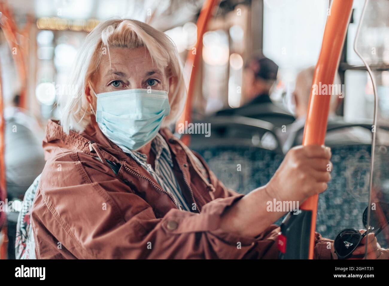 Una passeggero femminile di 40-50 anni che indossa una maschera chirurgica su un treno della metropolitana o un autobus durante il viaggio in una grande città durante il Covid 19 Foto Stock