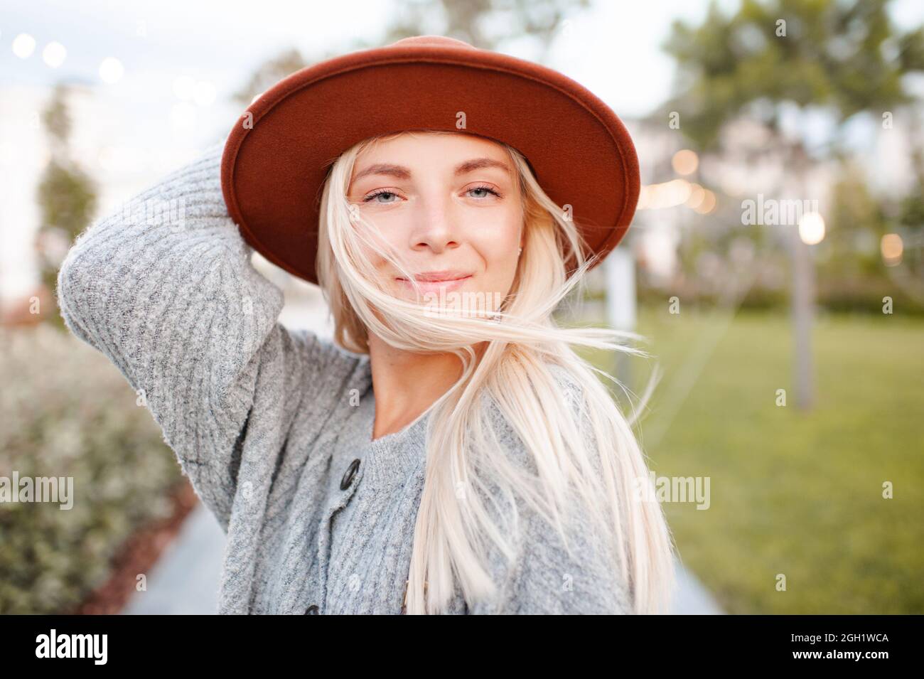 Bella bionda sorridente adulta ragazza 20-24 anni indossare abiti caldi casual e cappello in posa nel parco della città. Stagione autunnale. Signora romantica all'aperto. Lookin Foto Stock