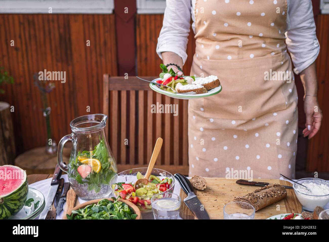 Gustatevi insalata di verdure fresche e baguette con formaggio caserario. Donna che serve cibo vegetariano sul piatto in occasione di una festa in giardino o di un evento di celebrazione Foto Stock