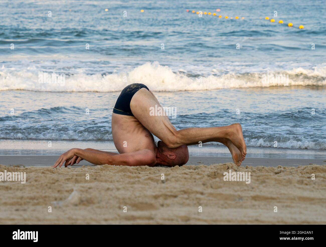 Un uomo in costume da bagno che flette il suo corpo su una spiaggia di sabbia. Foto Stock