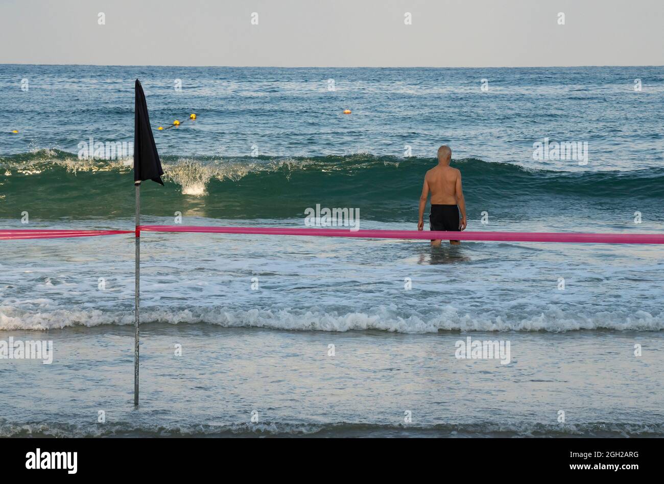 Un uomo che va per una nuotata nell'oceano, nonostante una bandiera nera e una linea rossa che avverte di non. Foto Stock