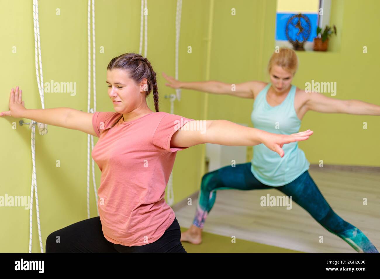 Due ragazze in abbigliamento sportivo stanno facendo yoga nella sala. Le donne eseguono asana difficili. Concetto di calma, equilibrio e concentrazione. Foto Stock