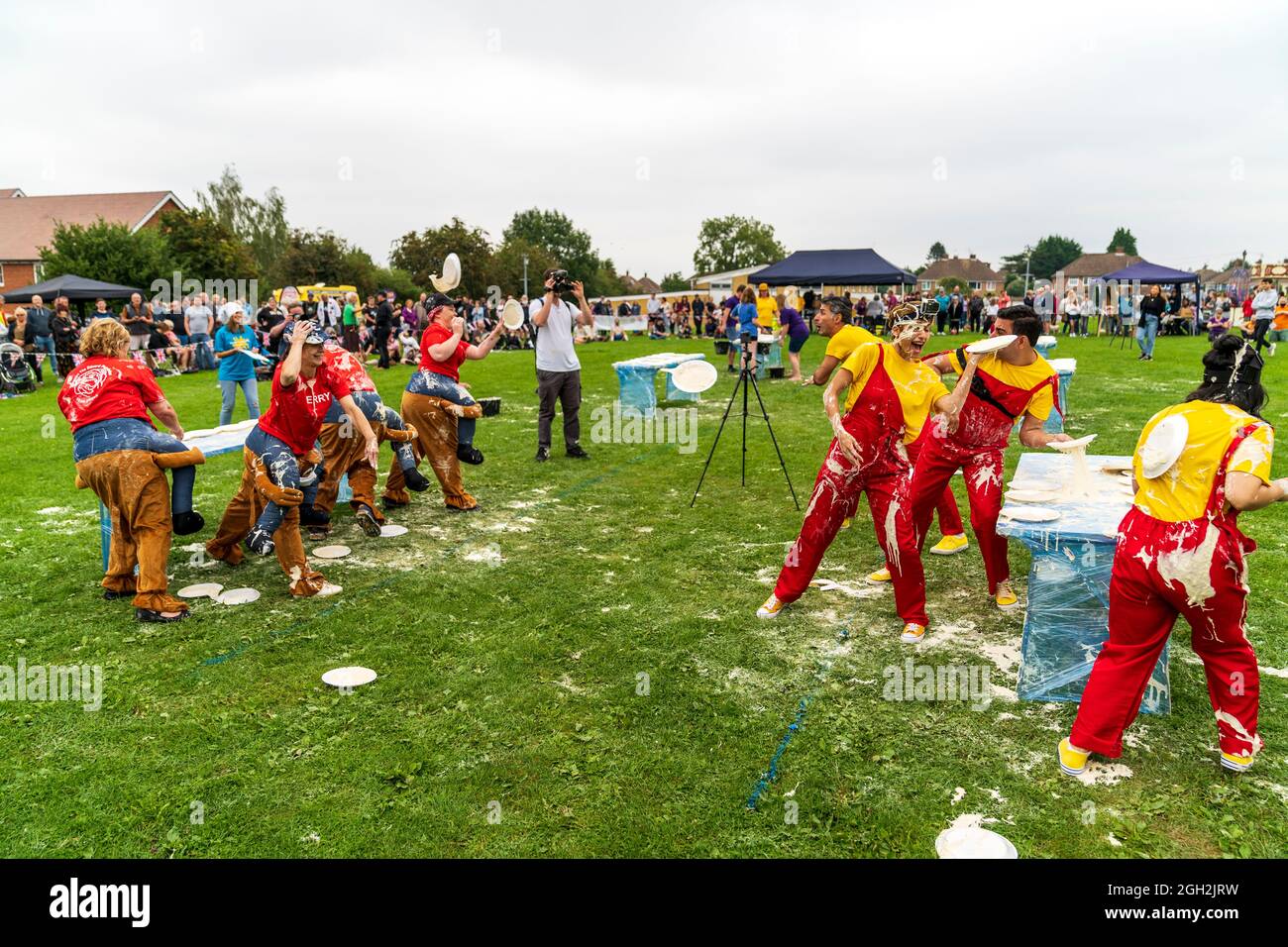 Due squadre di quattro ciascuno in abito fantasia, in un campo, gettando le torte di crema l'uno all'altro durante i campionati annuali della torta di crema di crema tenuti a Coxheath vicino Maidstone in Inghilterra con gli spettatori che guardano. Foto Stock