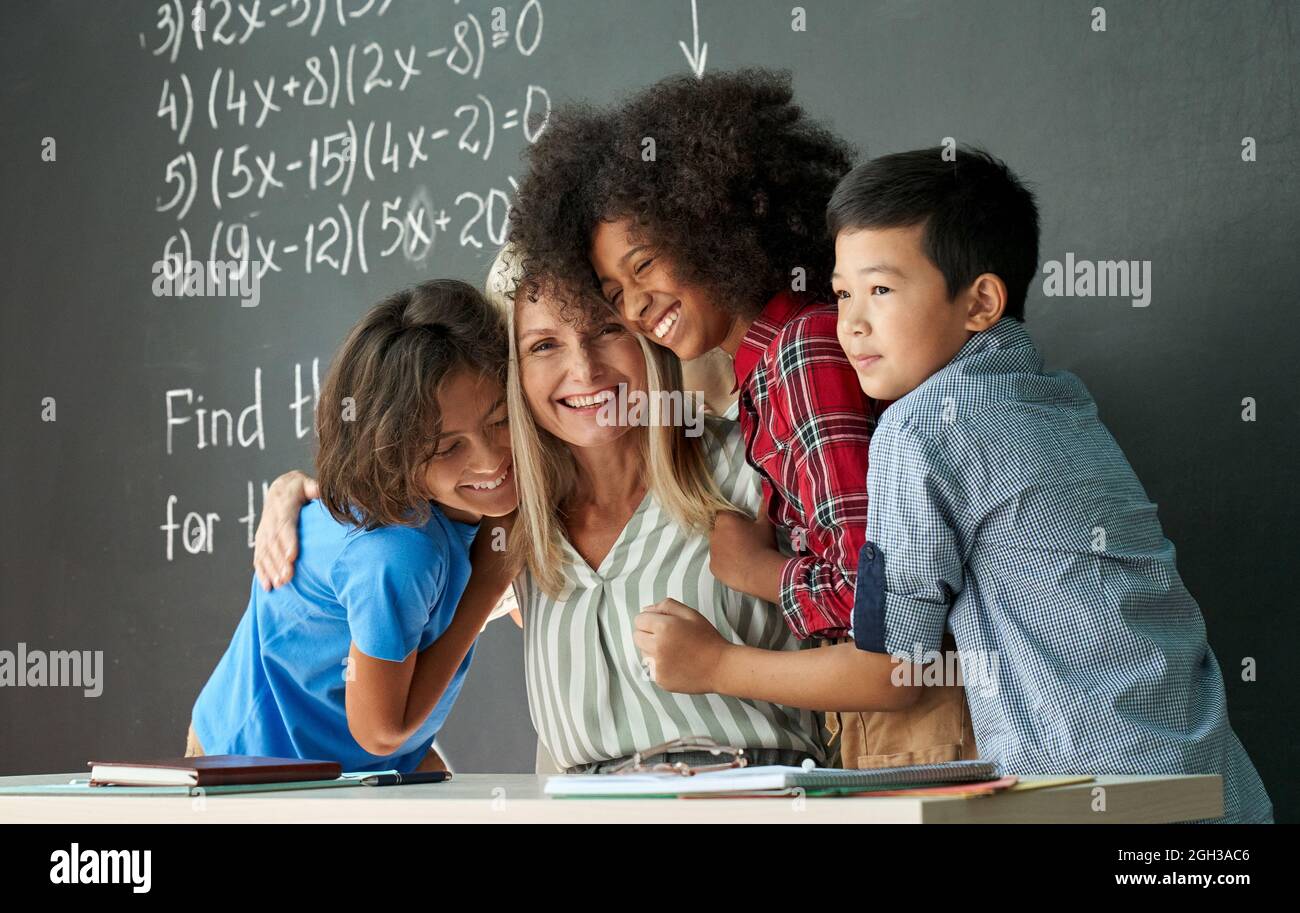 Felice diversi ragazzi scuola bambini studenti abbracciando l'insegnante femminile in classe. Foto Stock