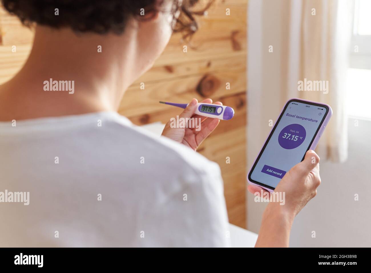 Una donna irriconoscibile scrive la sua temperatura basale sulla sua app per smartphone Foto Stock