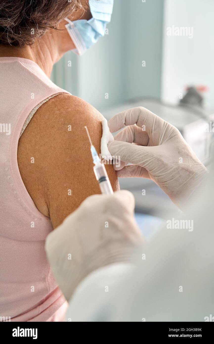 Donna anziana che indossa la maschera per il viso che riceve l'iniezione della vaccinazione. Foto Stock