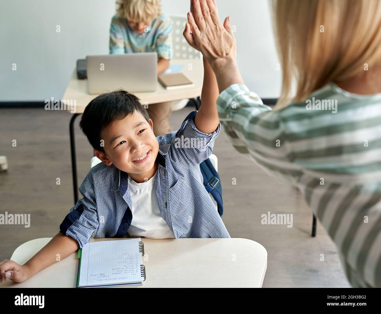 Ragazzo felice asiatico che dà alto cinque a insegnante femminile in classe. Foto Stock