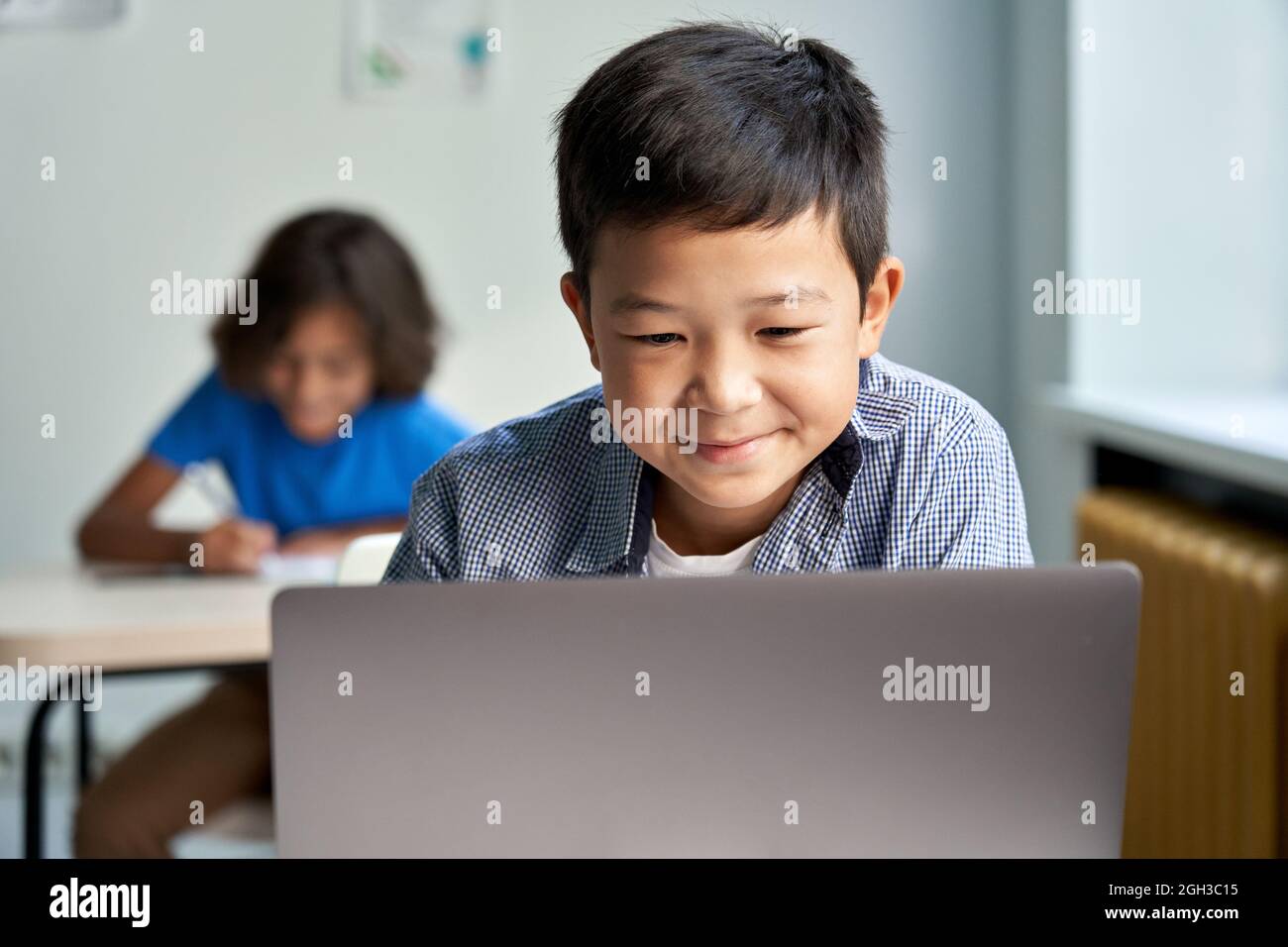 Felice ragazzo della scuola asiatica che usa il computer portatile in classe. Foto Stock