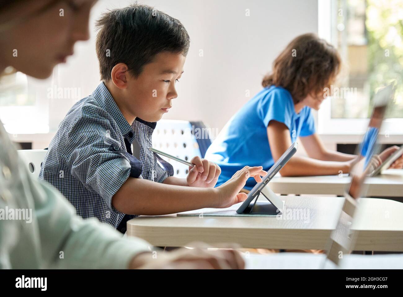 Ragazzo di scuola asiatico concentrato che usa il tablet digitale in classe. Foto Stock