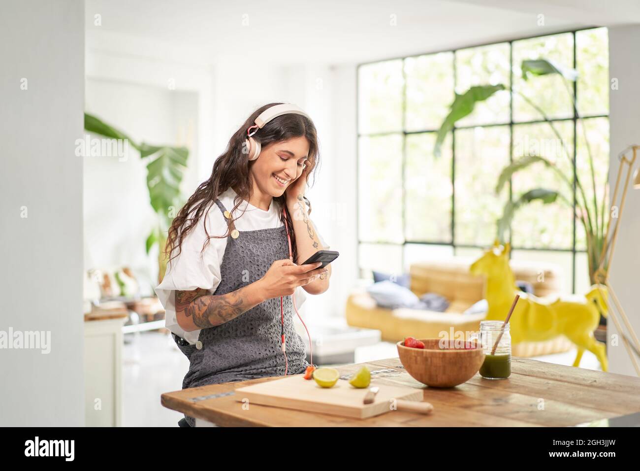 Bella giovane donna che ascolta la musica con le cuffie a casa al mattino facendo una sana colazione in un bel appartamento. Concetto di cibo sano. Foto Stock