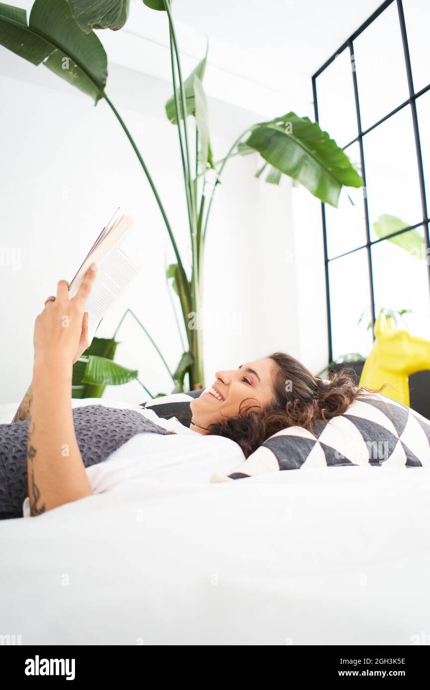 Giovane donna che legge un libro nella stanza accogliente, girare la pagina, imparare, studiare, istruzione, lettura di libri, concetto di soggiorno a casa e relax. Foto Stock