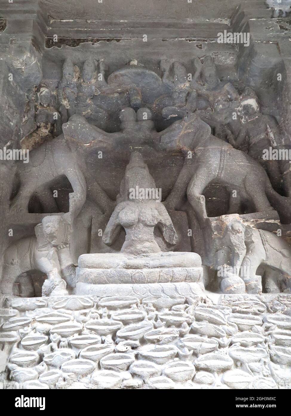 Intagliatura rupestre danneggiata di Lakshmi, la dea della ricchezza e aspetto principale della dea madre, seduta in padmasana su un trono di loto, Ellora Cave Foto Stock