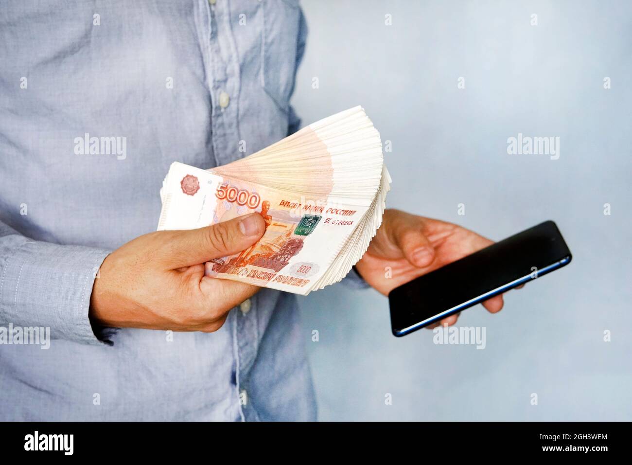 Giovane uomo detiene il denaro in mano e si preme lo schermo dello smartphone. Guadagna denaro attraverso il mobile app. Business via smartphone. Foto Stock