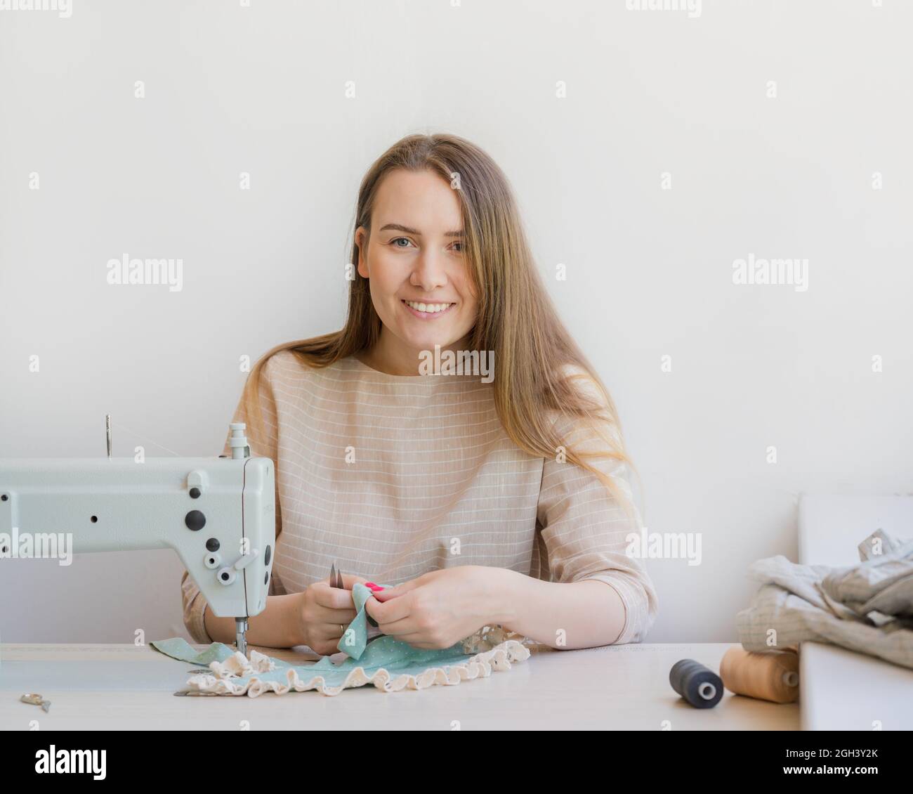 Felice atelier donna proprietario che lavora sul posto di lavoro con la macchina da cucire Foto Stock